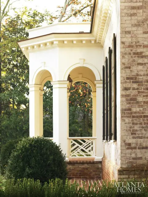 Traditional brick home with a white arched portico, dark shutters, and lush green landscaping.