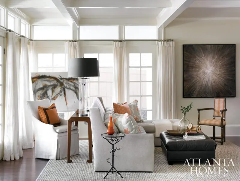 Living room with sectional sofa, slipcovered armchair, black leather ottoman, and abstract art on wall.