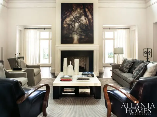 Living room with fireplace, large abstract art, neutral upholstered seating, dark leather armchairs, and a white coffee table with books and vases.