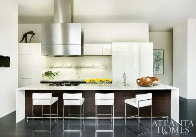 Modern white kitchen with dark wood island, four white leather bar stools, stainless steel range hood, and abstract art on the wall.