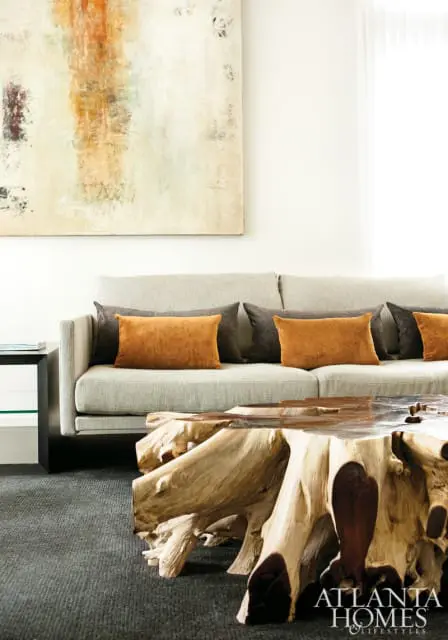 Living room with a light gray sofa adorned with burnt orange and charcoal pillows, a large abstract painting on the wall, and a unique live-edge wood coffee table.