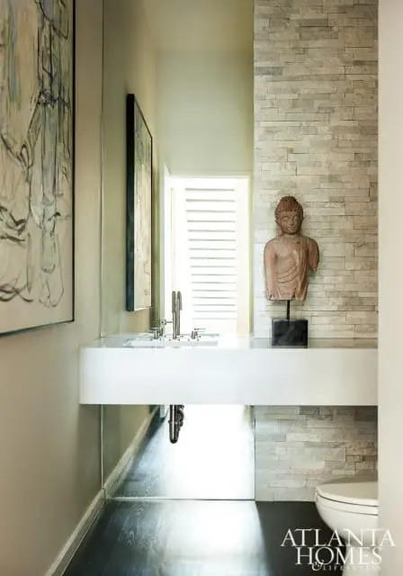 Modern bathroom with a floating white vanity, stacked stone accent wall, Buddha bust, and abstract art.