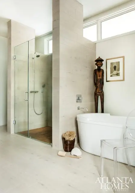 Modern bathroom with glass-enclosed shower, freestanding tub, light wood-look tile, and a wooden statue