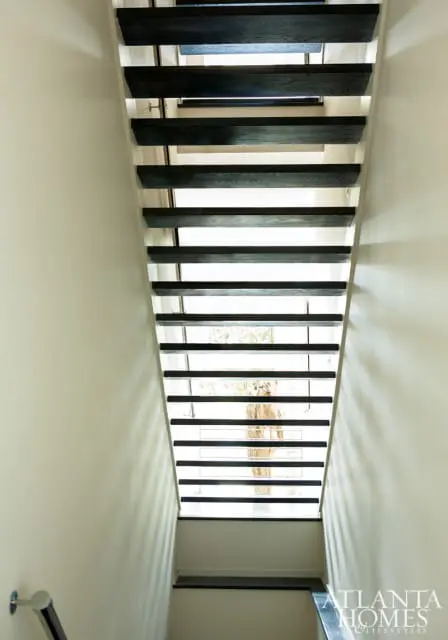 Modern staircase with dark wood treads and white walls, featuring a glass railing and natural light filtering through.