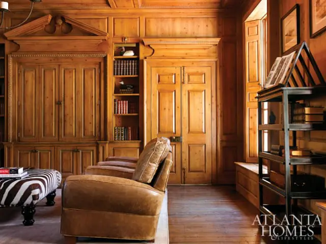 Library with warm wood paneling, built-in bookshelves, leather armchairs, and a zebra-print ottoman.