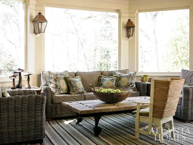 Sunroom with wicker furniture, patterned throw pillows, a rustic wood coffee table with a bowl of green apples, and striped rug.