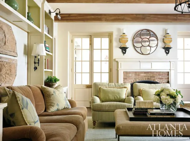 Living room with brown sofa, green striped armchair, white fireplace with brick surround, and French doors.