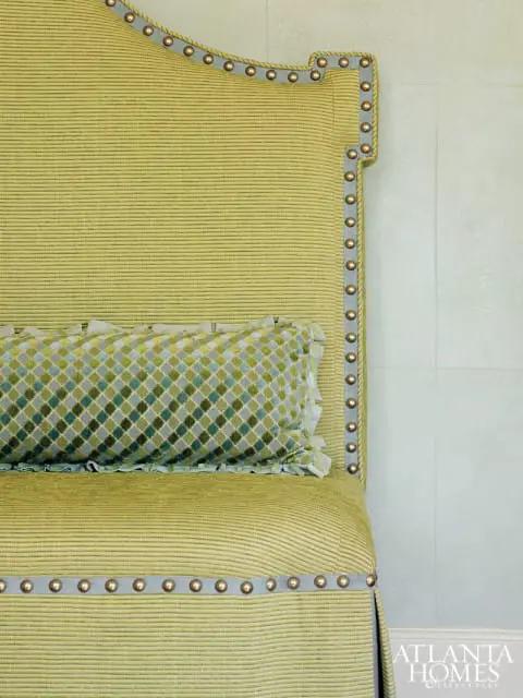 Headboard and seat of a chair upholstered in textured lime green fabric, accented with nailhead trim and a diamond-patterned bolster pillow.
