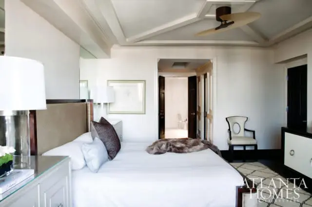 Bedroom with a king-size bed, upholstered headboard, white bedding, and a faux fur throw. A ceiling fan is visible above.