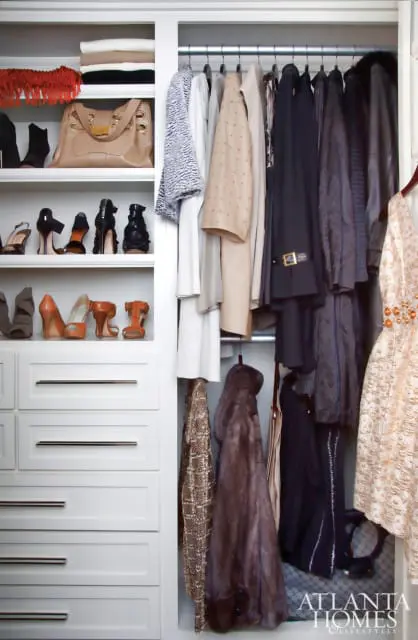 White closet with shelves holding folded clothes, handbags, and shoes, and hanging garments including coats, a fur jacket, and a beaded dress.