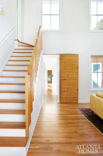 Modern entryway with white walls, a wooden staircase with white risers, a slatted wood barn door, and light wood floors.