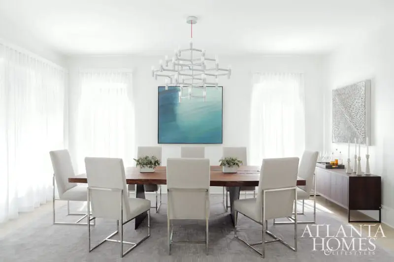 Modern dining room with a live-edge wood table, upholstered chairs with chrome frames, a geometric chandelier, and abstract blue wall art.