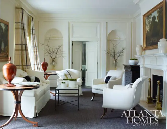 Living room with white slipcovered sofa and armchairs, dark wood side tables, fireplace, and plaid curtains.