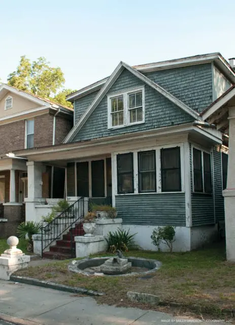 Two-story house with gray wood siding and shingles, a covered porch with white columns, and a dormer window.