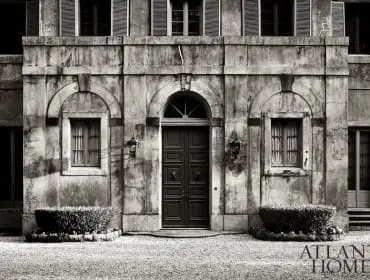 Stone building facade with arched windows, shutters, and a dark double door. Atlanta Homes logo.