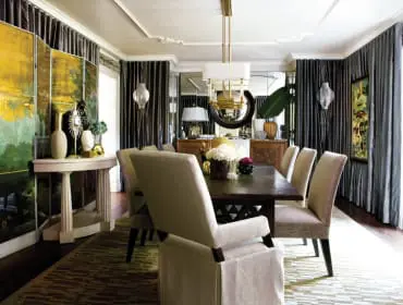 Dining room with dark wood table, upholstered chairs, ornate screen, mirrored walls, and dark gray floor-to-ceiling curtains.