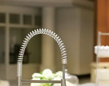 Brushed nickel kitchen faucet with a coiled spring spout over a light gray countertop and stainless steel sink.
