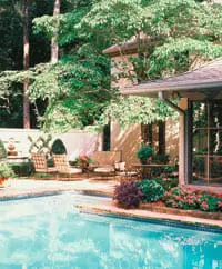 Tuscan-style home with stucco exterior and arched windows, featuring a swimming pool and manicured garden with lounge chairs and a sofa.