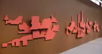 Abstract red wall art mounted on a brown wall, depicting stylized shapes resembling buildings and planes.