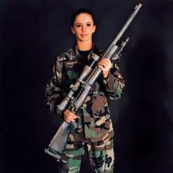 Woman in camouflage uniform holding a scoped rifle against a dark background.