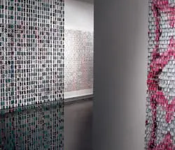 Close-up of a wall covered in small, square mosaic tiles in shades of teal and pink, with a reflective floor mirroring the pattern.