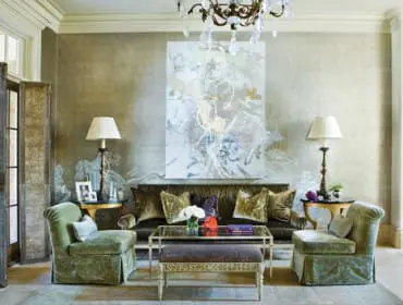 Living room with plush green velvet armchairs, a dark sofa with gold pillows, a glass coffee table, and a large abstract painting on a textured wall.