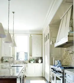 Cream kitchen with white custom cabinetry, a large stainless steel range, marble backsplash, and a dark wood island with a granite countertop. Three pendant lights hang over the island.