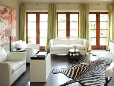 Living room with white sofas, a zebra hide rug, light green curtains, and large wooden French doors.