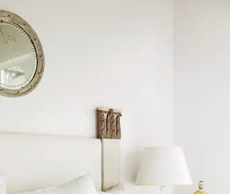 White upholstered headboard with decorative wooden accents, topped with white pillows and a yellow patterned accent pillow. A round mirror hangs on the wall above.