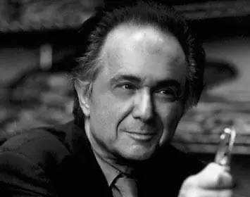 Black and white portrait of a man in a suit and tie, holding a small object in his right hand.