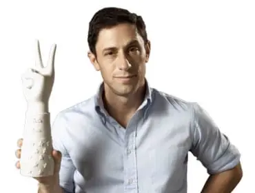 Man in light blue button-down shirt and white pants holding a white ceramic hand sculpture with stars and a peace sign
