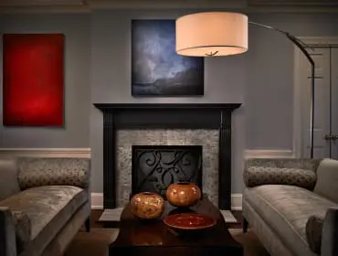 Living room with gray walls, a black fireplace with mosaic tile surround, two velvet chaise lounges, and abstract art above the fireplace.
