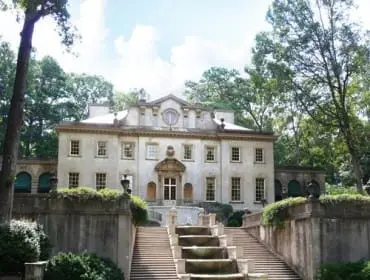 Classical style mansion with a grand staircase and tiered fountain leading to the entrance, surrounded by lush green lawns and mature trees.