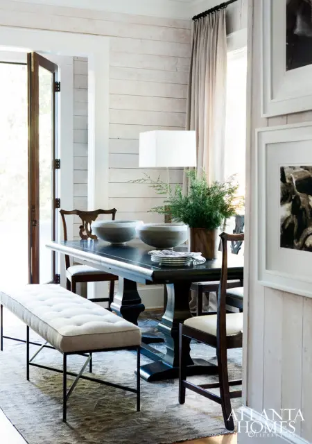 Dining room with a dark wood table, tufted bench, wooden chairs, and a white plank wall.