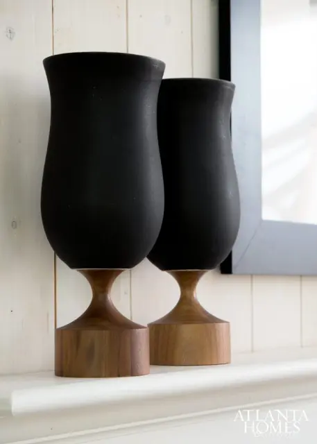 Two black matte vases with curved bodies sit on wooden pedestals with square bases.