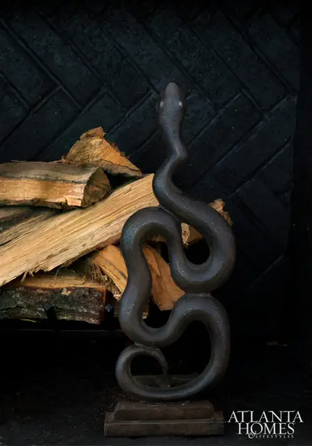 Dark metal snake sculpture in front of stacked firewood and a black brick fireplace surround.