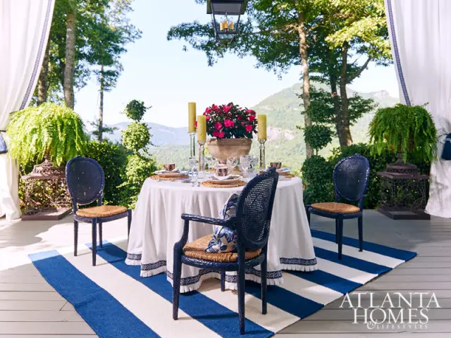 Covered porch with a round dining table set for four, navy cane-back chairs, and a mountain view.