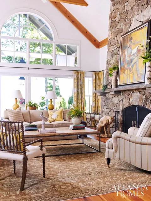 Living room with vaulted ceiling, large stone fireplace, arched windows, neutral sofa, and patterned curtains.
