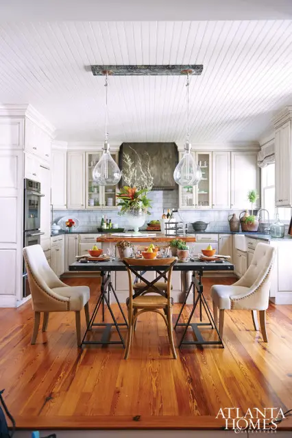 Kitchen with white beadboard ceiling, cream cabinetry, marble subway tile backsplash, and a dining table set for four with upholstered chairs and cross-back chairs.