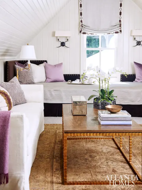 Living room with white sofa, built-in daybed, wood coffee table, and oriental rug. Accents of purple pillows and a white orchid arrangement.