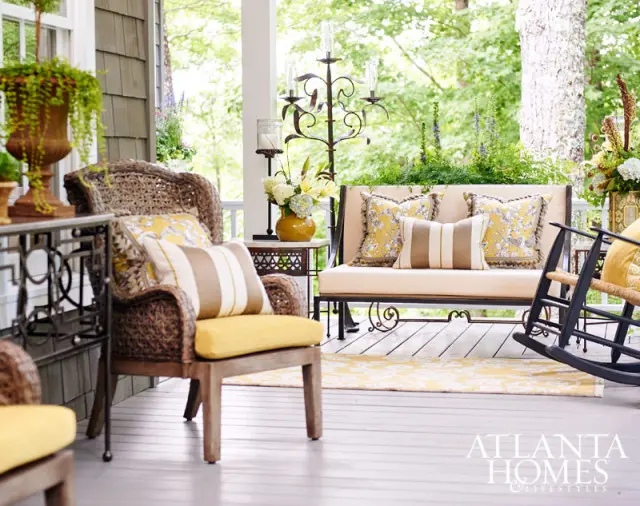 Covered porch with wicker chairs, a loveseat, and a rocking chair, all adorned with yellow and brown patterned cushions.