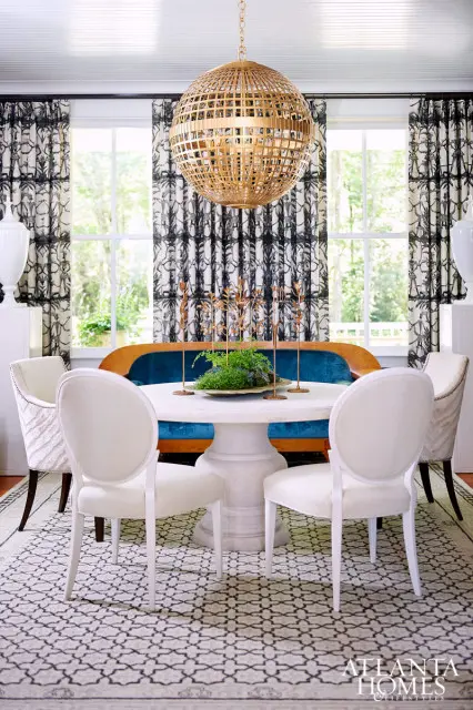 Dining room with white pedestal table, blue velvet banquette, white upholstered chairs, and a large gold orb chandelier.