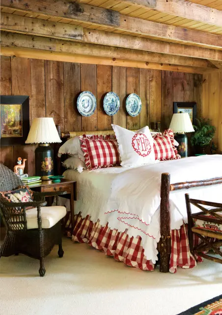 Bedroom with rustic wood paneled walls and ceiling, a bed with white linens and red gingham accents, and wicker furniture.