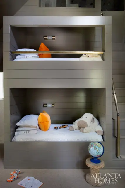 Bunk beds with gray shiplap walls, white bedding, orange pillows, and stuffed animals. A globe sits on a cork stool beside the lower bunk.