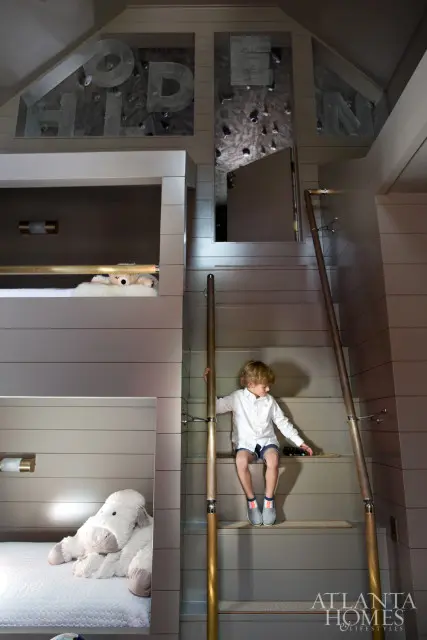 Boy sitting on stairs in a room with bunk beds and large letters spelling "HOLDEN" above a climbing wall.