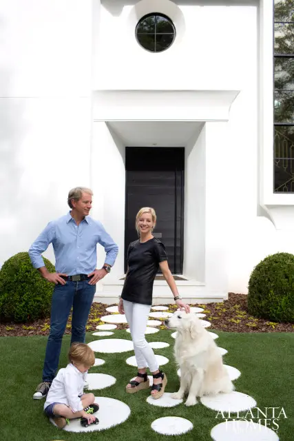 A family and their dog pose in front of a modern white house with a black door and circular window.