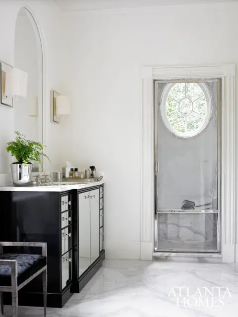 White bathroom with a black vanity featuring mirrored cabinet doors, a marble countertop, and a chrome-framed oval shower with a window view.