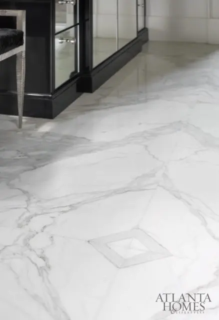 White marble flooring with gray veining and a geometric inlay detail. A black mirrored cabinet and a silver-legged chair with black upholstery are partially visible.