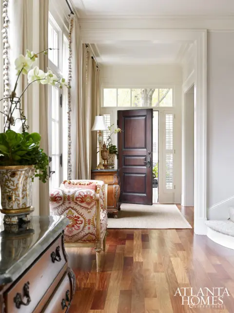 Entryway with dark wood double doors, patterned armchair, ornate table lamp, and hardwood floors.