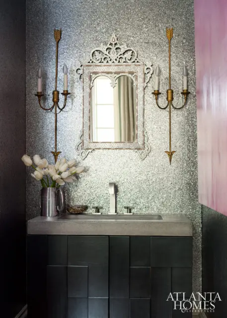 Powder room with a silver speckled wallpaper, a concrete vanity with a dark wood cabinet, a silver faucet, a decorative mirror, and gold sconces.